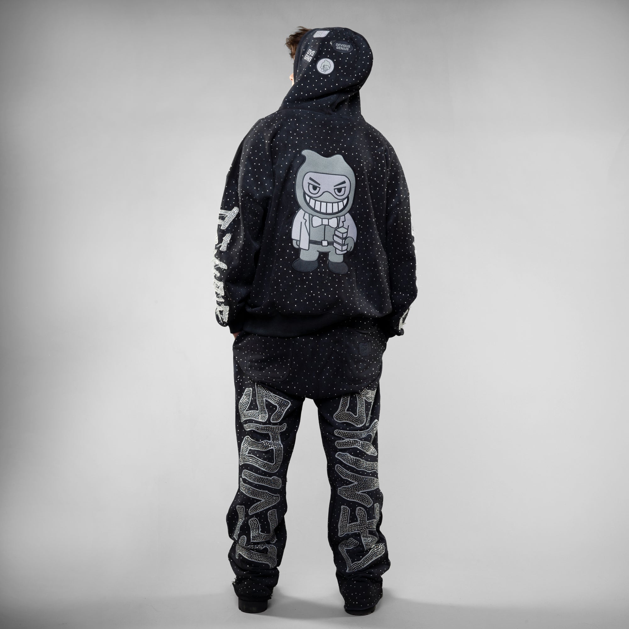Person wearing a black hoodie and pants with graphic designs on a gray background