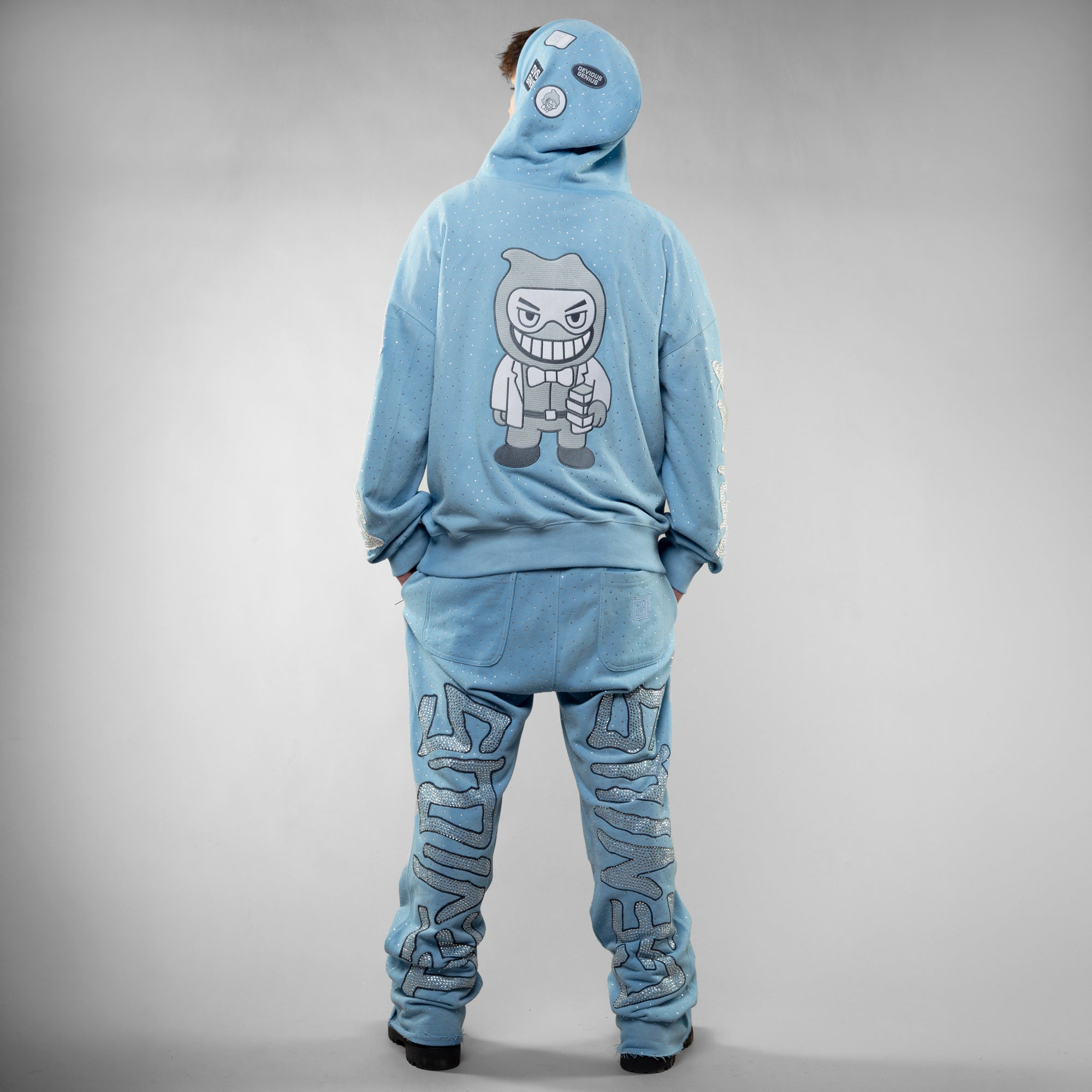 Person wearing a blue tracksuit with a character design on the back against a gray background